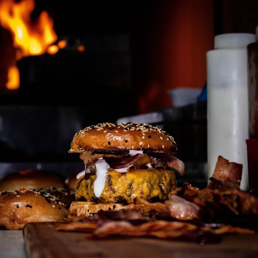 Hambúrguer artesanal com bacon e queijo em frente ao forno a lenha
