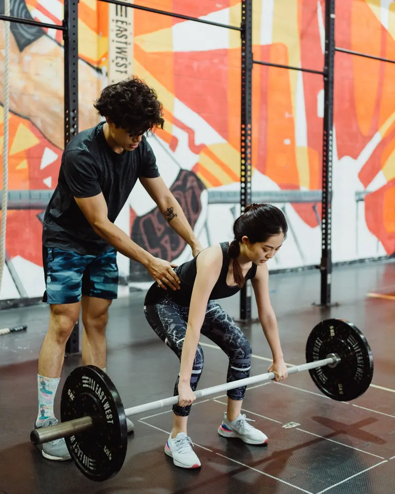 Personal trainer corrigindo a postura de aluna no levantamento de peso